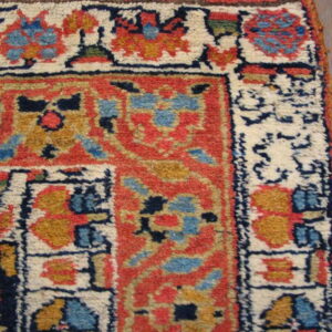 High-pile rug corner detail with bold red, cream, blue, and gold geometric patterns visible on wood floor.