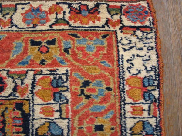 High-pile rug corner detail with bold red, cream, blue, and gold geometric patterns visible on wood floor.