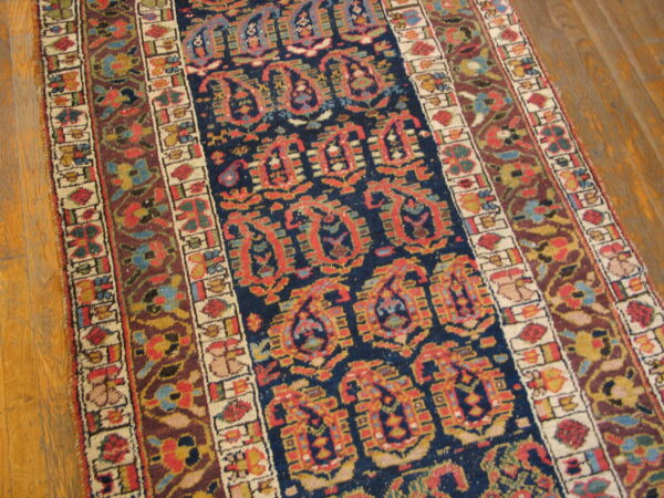 Navy, red, and maroon runner rug featuring boteh and floral borders on light brown hardwood planks.