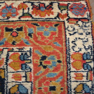 Rug corner with intricate red, cream, blue, and gold motifs and high pile on wood planks.