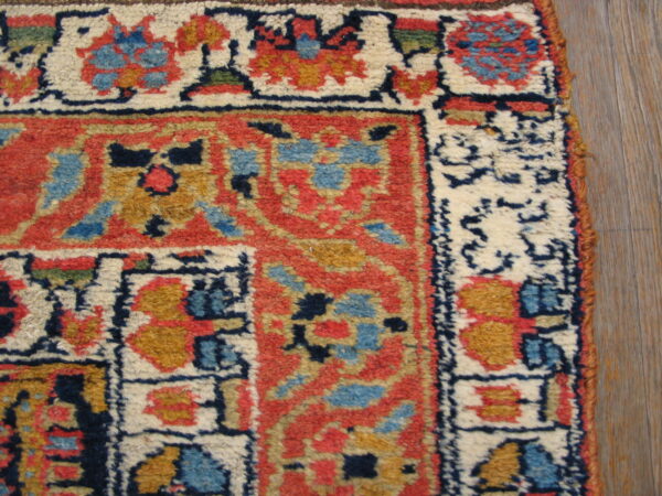 Rug corner with intricate red, cream, blue, and gold motifs and high pile on wood planks.