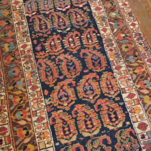 Low-pile rug with a detailed navy and red central pattern, complex borders, laid over light brown wood planks.