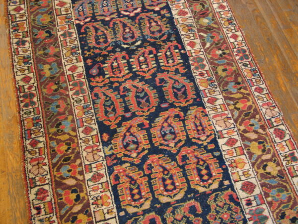 Low-pile rug with a detailed navy and red central pattern, complex borders, laid over light brown wood planks.