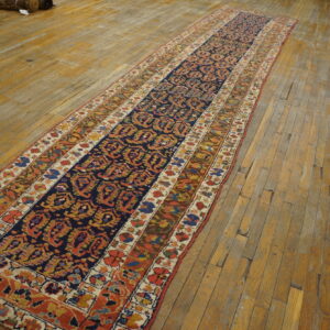 Traditional runner rug featuring a navy central field and multicolored borders lies on distressed wood planks.
