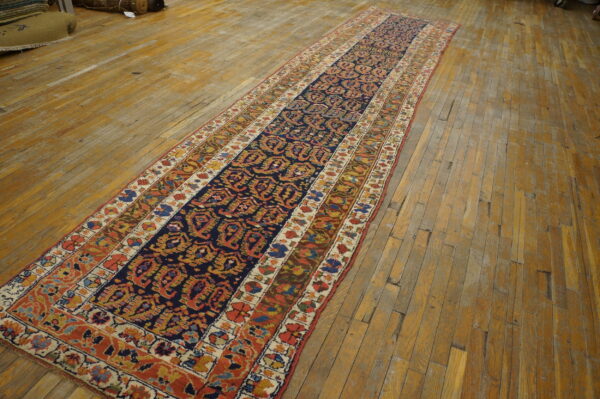 Traditional runner rug featuring a navy central field and multicolored borders lies on distressed wood planks.