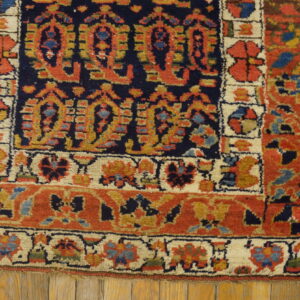 Navy, rust, and cream rug with complex geometric patterns resting on light brown wood flooring.