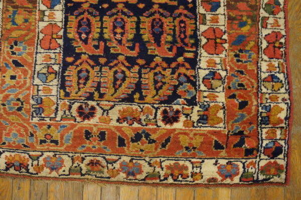 Navy, rust, and cream rug with complex geometric patterns resting on light brown wood flooring.