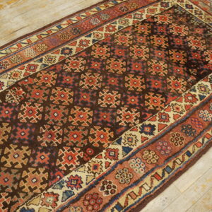 A dark brown runner rug with red, blue, and beige geometric patterns lies on light, distressed wood planks.