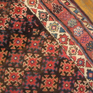 Geometric red, blue, and cream patterned rug with a dark field, partially resting on a wooden floor.