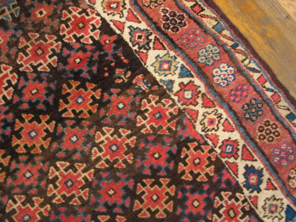 Geometric red, blue, and cream patterned rug with a dark field, partially resting on a wooden floor.