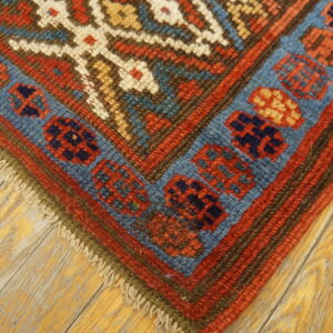 Geometric red and blue border design on a low pile rug resting on distressed hardwood planks.