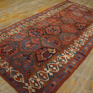 Geometric rust, navy, and teal rug with complex borders displayed on distressed wooden flooring.