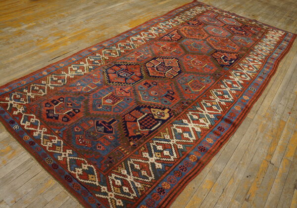 Geometric rust, navy, and teal rug with complex borders displayed on distressed wooden flooring.