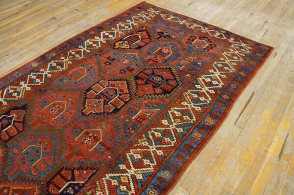 Red and blue tribal-style rug with complex geometric medallions on distressed blonde hardwood flooring.
