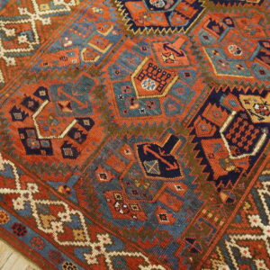 Low-pile geometric rug in rust, navy, teal, and brown lies on distressed wood flooring.