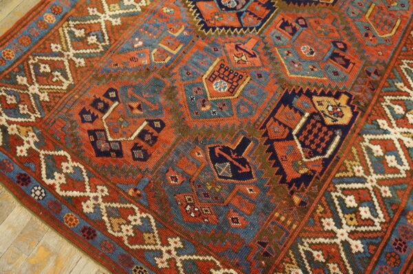 Low-pile geometric rug in rust, navy, teal, and brown lies on distressed wood flooring.