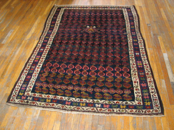 Deep navy rug featuring repeating red and pink gul motifs, multicolored borders, resting on polished hardwood.
