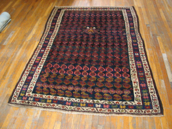 Rectangular rug featuring a dark blue field, red geometric patterns, and colorful borders, displayed on wood plank flooring.