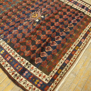 Dark geometric rug with red repeating medallions and colorful layered borders rests on light wood floors.