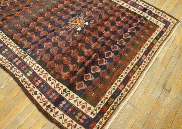 Dark geometric rug with red repeating medallions and colorful layered borders rests on light wood floors.