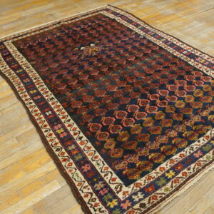 Rectangular rug with a navy and red geometric pattern and multi-colored border on light distressed wood flooring.
