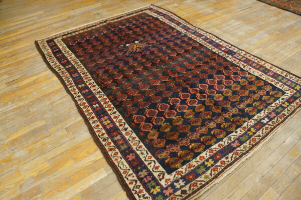 Rectangular rug with a navy and red geometric pattern and multi-colored border on light distressed wood flooring.