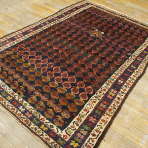 Traditional dark rug with red repeating patterns and colorful borders placed on worn light wood flooring.