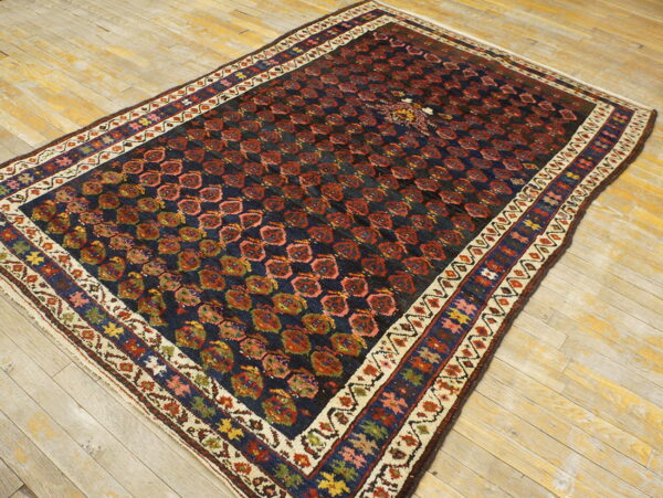 Traditional dark rug with red repeating patterns and colorful borders placed on worn light wood flooring.