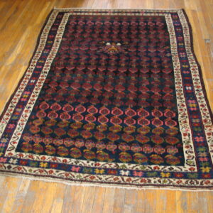 Navy and red patterned rug with detailed colorful borders lies on wide-plank, glossy, worn hardwood flooring.