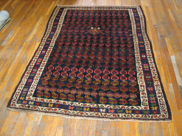Navy and red patterned rug with detailed colorful borders lies on wide-plank, glossy, worn hardwood flooring.