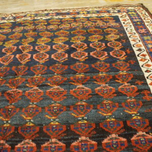 Dark blue rug with rust, blue, and yellow motifs and a patterned cream border on wood flooring.