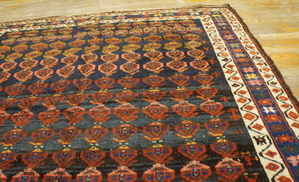 Dark blue rug with rust, blue, and yellow motifs and a patterned cream border on wood flooring.
