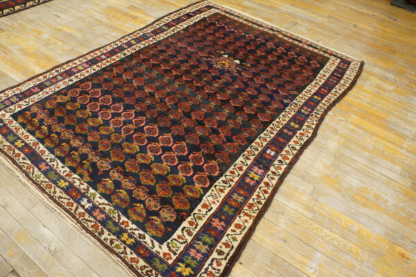 Navy low-pile rug with repeating red geometric guls and a multicolored border on light distressed wood floors.