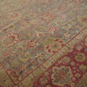 Ornate low-pile rug with a pale blue-gray floral field contrasting a wide red and gold border.