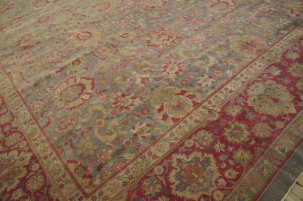 Ornate low-pile rug with a pale blue-gray floral field contrasting a wide red and gold border.