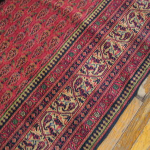 Deep red patterned rug with detailed borders in navy, gold, and green rests on wood planks.