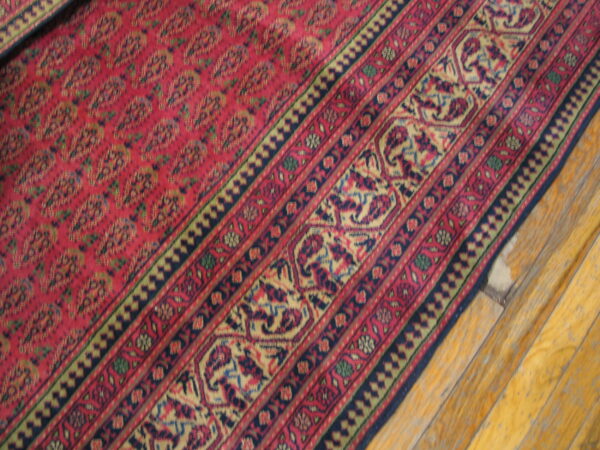 Deep red patterned rug with detailed borders in navy, gold, and green rests on wood planks.