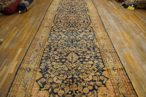 Navy runner with detailed gold and pink floral patterns covers aged yellow hardwood flooring.