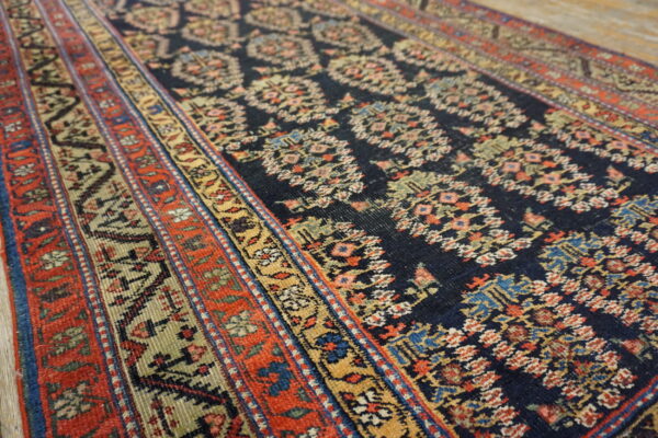 Close-up of a runner rug with a navy floral core pattern and red, gold, and blue striped borders.