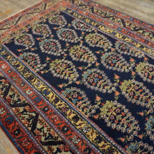Navy blue rug with a repeating multi-color motif and elaborate red, gold, and blue banded borders.