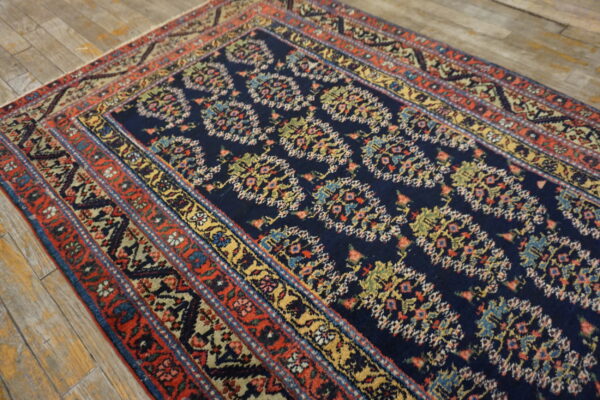Navy blue rug with a repeating multi-color motif and elaborate red, gold, and blue banded borders.