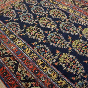 Navy rug featuring an intricate colorful floral pattern and multi-banded red border on worn wood flooring.