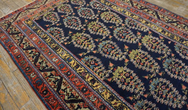 Navy rug featuring an intricate colorful floral pattern and multi-banded red border on worn wood flooring.