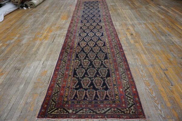 Low-pile navy runner featuring geometric motifs and red borders lies on rustic, worn wood plank flooring.