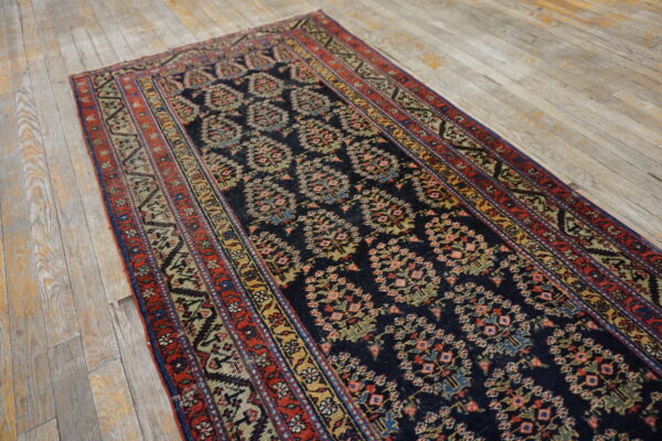 Navy runner rug with repeating pink and green medallions and red borders on light rustic wood floor.