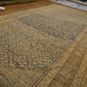 A large, distressed traditional rug with navy blue and tan patterns lies on a worn wooden floor.