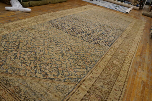 A large, distressed traditional rug with navy blue and tan patterns lies on a worn wooden floor.