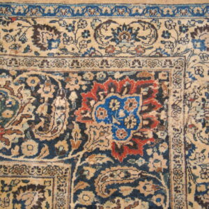 Intricate low-pile rug detail showing beige, navy blue, red, and royal blue floral patterns and borders.