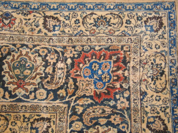 Intricate low-pile rug detail showing beige, navy blue, red, and royal blue floral patterns and borders.
