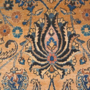 Intricate floral and vine pattern rug detail in shades of ochre, navy blue, black, and light brown.